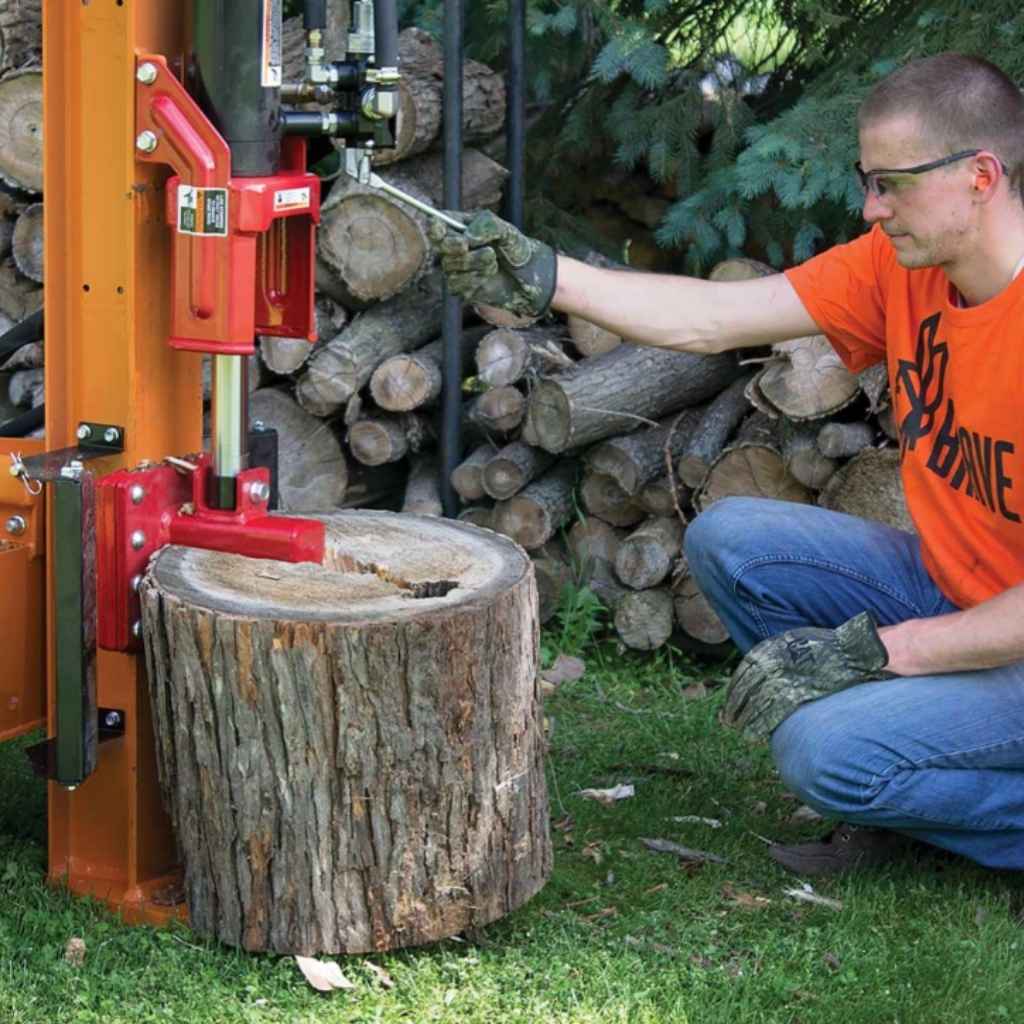 Person using a brave 24 ton log splitter with a stack of logs in the background
