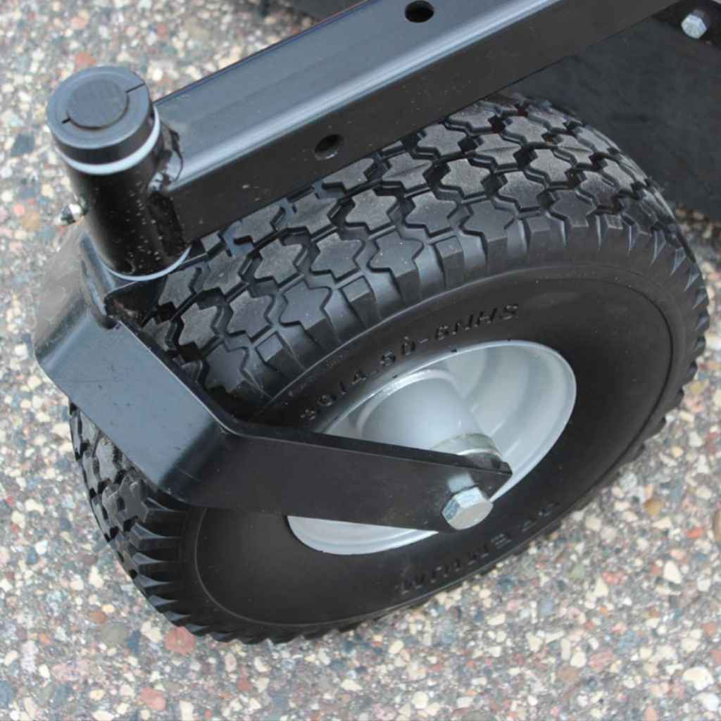 Close-up of a large wheel with of a brave pro rough cut mower with a black tire and silver hub on a textured surface.