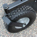 Close-up of a large wheel with of a brave pro rough cut mower with a black tire and silver hub on a textured surface.