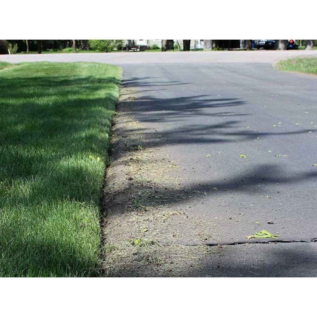 Green grass edged by a brave pro 10 inch lawn edger next to a paved road with tree shadows