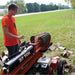 Person operating a brave pro towable 37-ton log splitter outdoors on a grassy area.