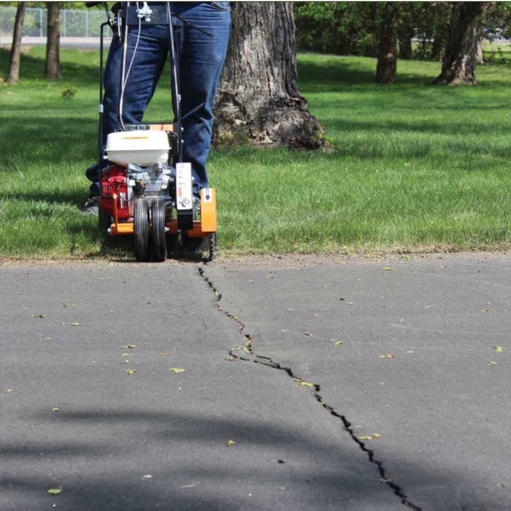 Person using an Orange Brave Crack Cleaner on a grassy area with trees in the background