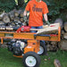 Person using a brave 24 ton log splitter with a stack of logs and trees in the background