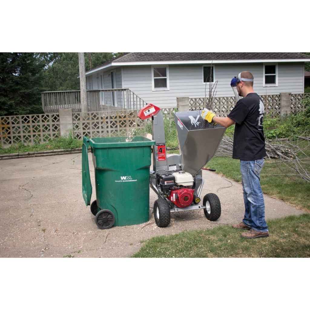 Person using a dosko brush chipper with a green trash bin outdoors.