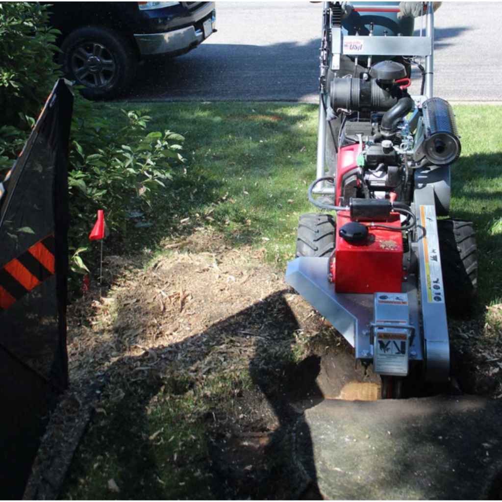 dosko self propelled 20 hp Stump grinder in use on a tree stump with a vehicle and grass in the background.
