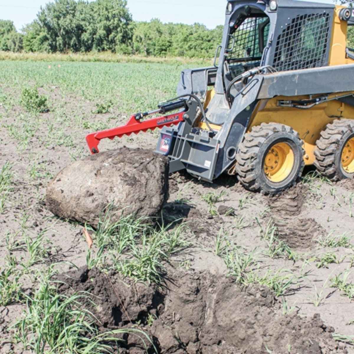 Skid steer loader with a greywolf Skid steer rock devil with a large rock in a field