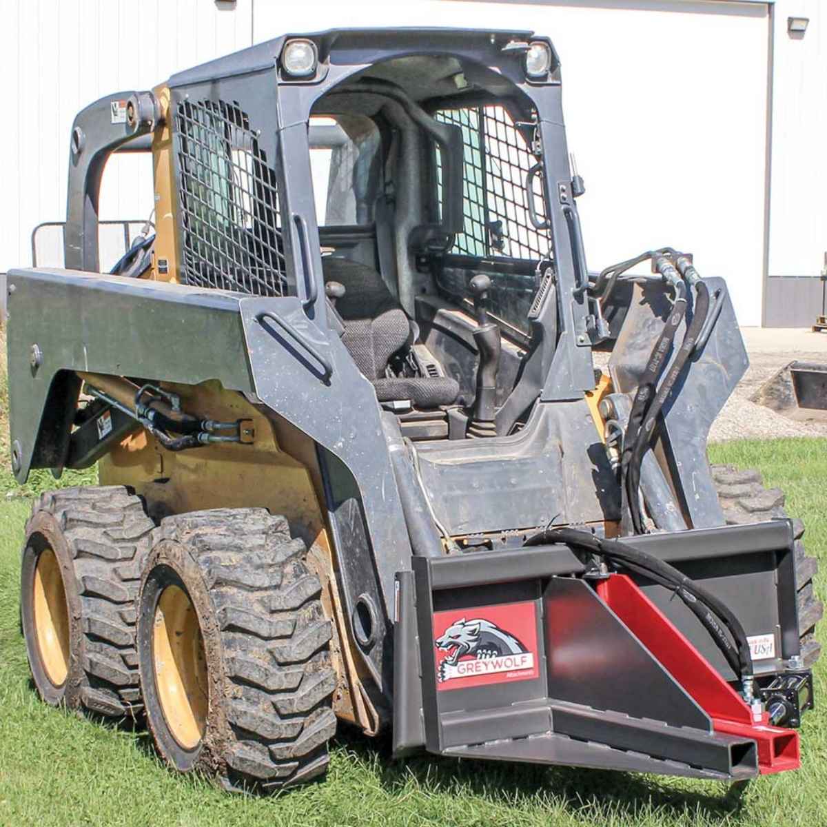 Skid steer loader with a Greywolf skid loader tree puller on grass