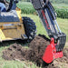 Skid Steer with a GREYWOLF backhoe attachment digging into the ground in an agricultural setting.