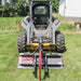 Skid steer loader with a Greywolf Rock Devil attachment on grassy terrain