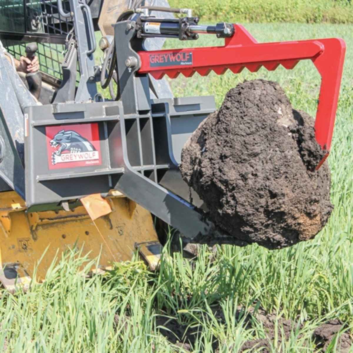 Greywolf Skid Steer Rock Devil lifting a large rock in a grassy area, with 'GreyWolf' branding visible.