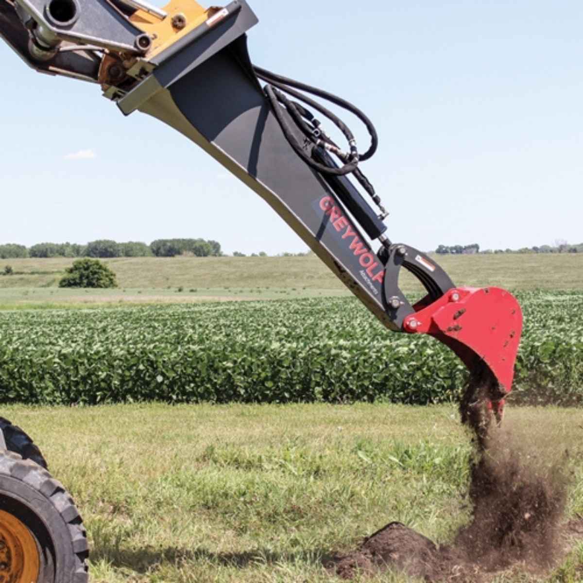 greywolf Backhoe attachment digging into the ground with a field in the background