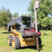 Person operating a skid steer loader with a Greywolf tree puller attachment handling a post in a grassy area.