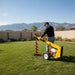 Person using a groundhog 1m5c auger in a backyard with mountains in the background