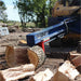 Blue iron and oak 24 ton skid mount log splitter attached to a skid loader splitting a log with trees in the background during the daytime.