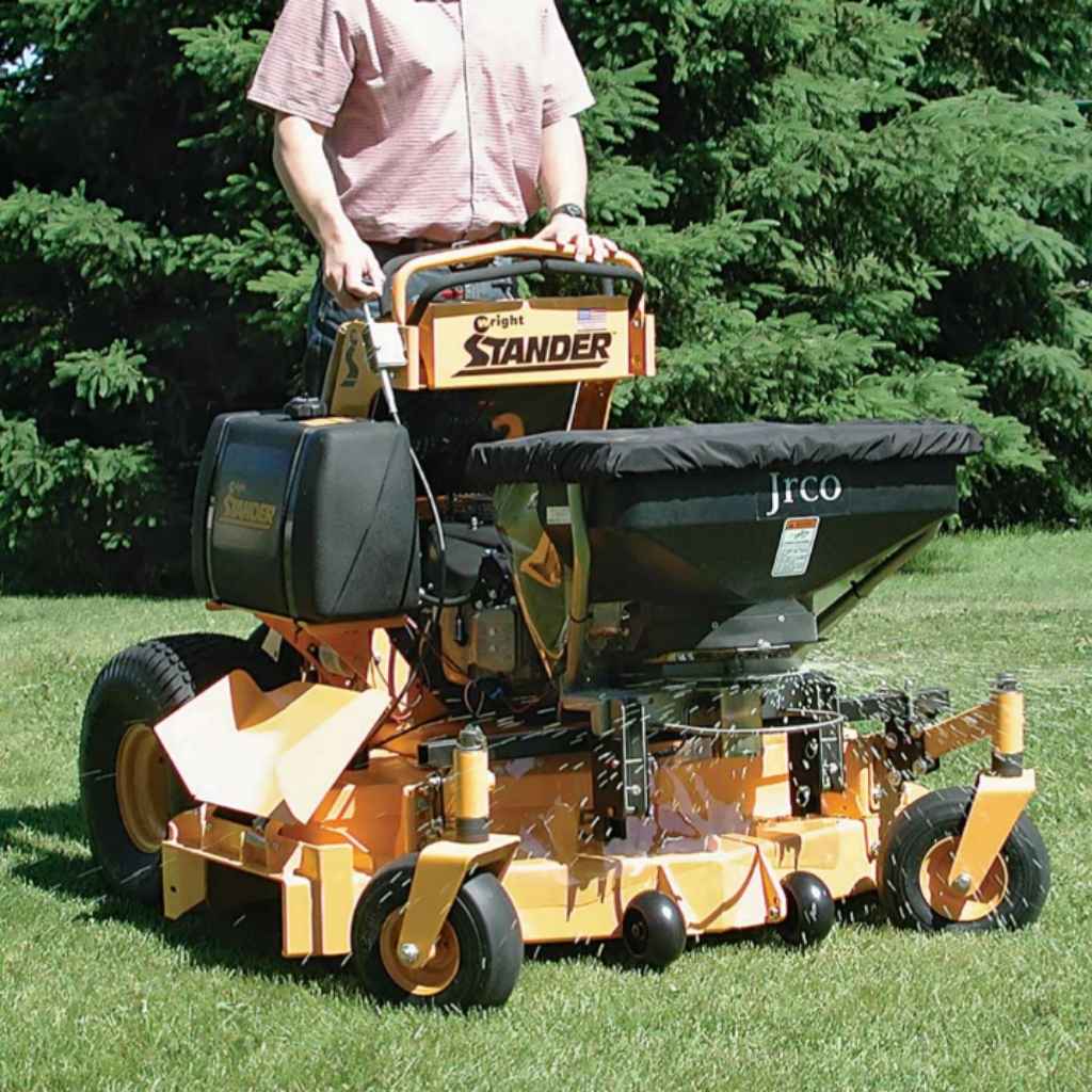 Person operating a Jrco Broadcast spreader 504 cable control on grass with trees in the background