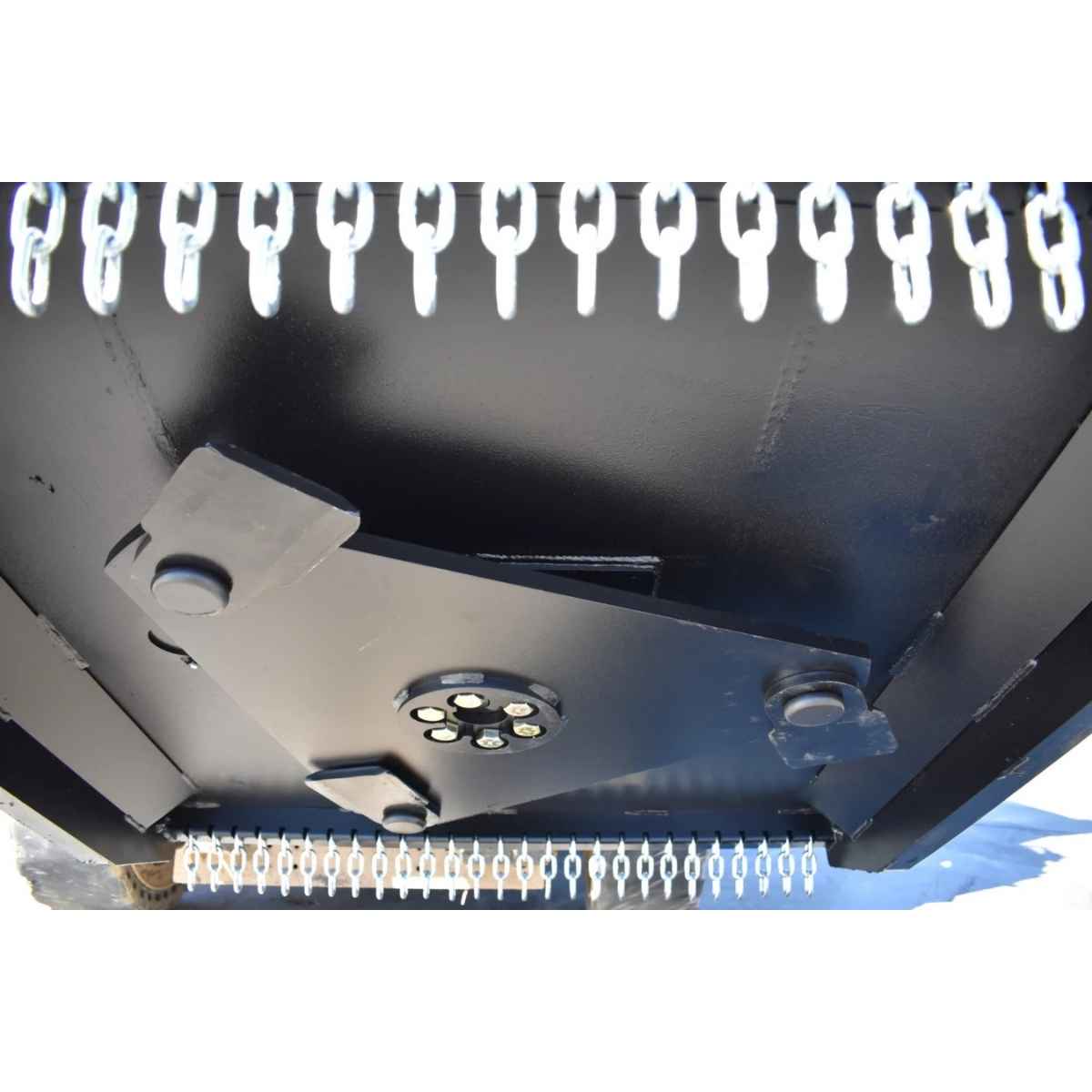 Close-up of the underside of a black loflin closed front brush cutter, showing mounting brackets, a circular light fixture, and rows of white plastic or metal links along the top and bottom edges.