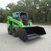 Green skid steer loader with a loflin trash bucket on a paved surface with trees in the background.