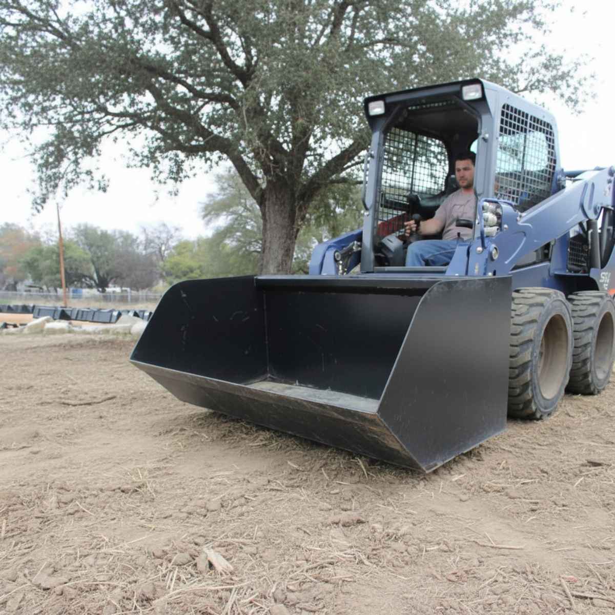 Skid steer loader with a loflin trash bucket on a construction site with a person inside