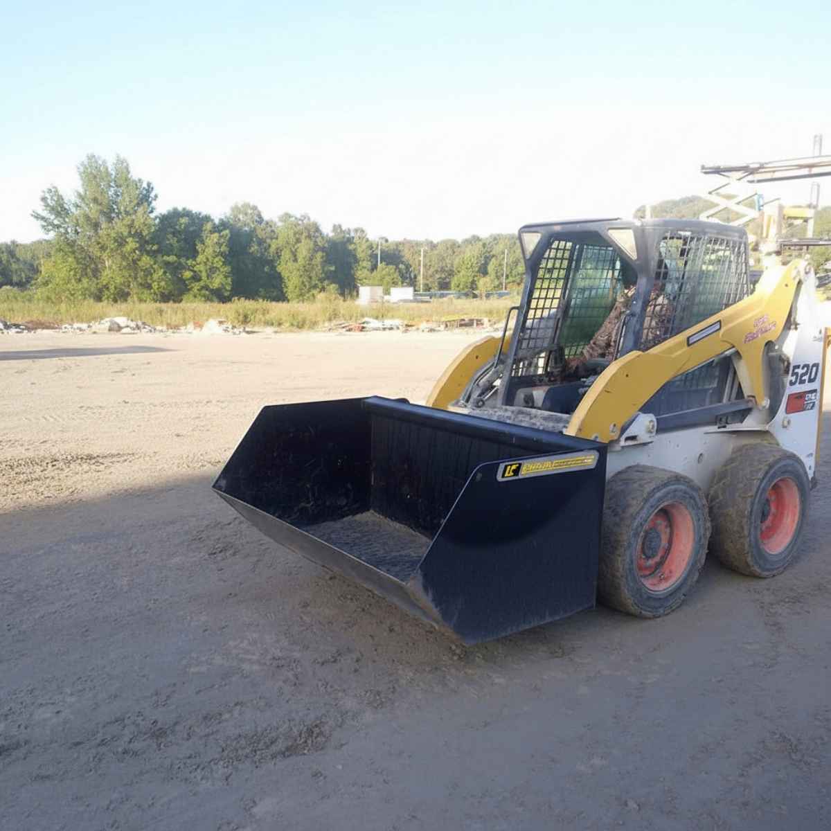 Skid steer loader with a loflin skid steer trash bucket on a construction site with trees in the background