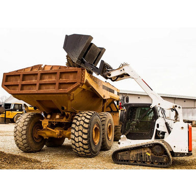 mini skid steer dumping material into dump truck using the loflin front dump bucket on a gravel floor with a factory in the background