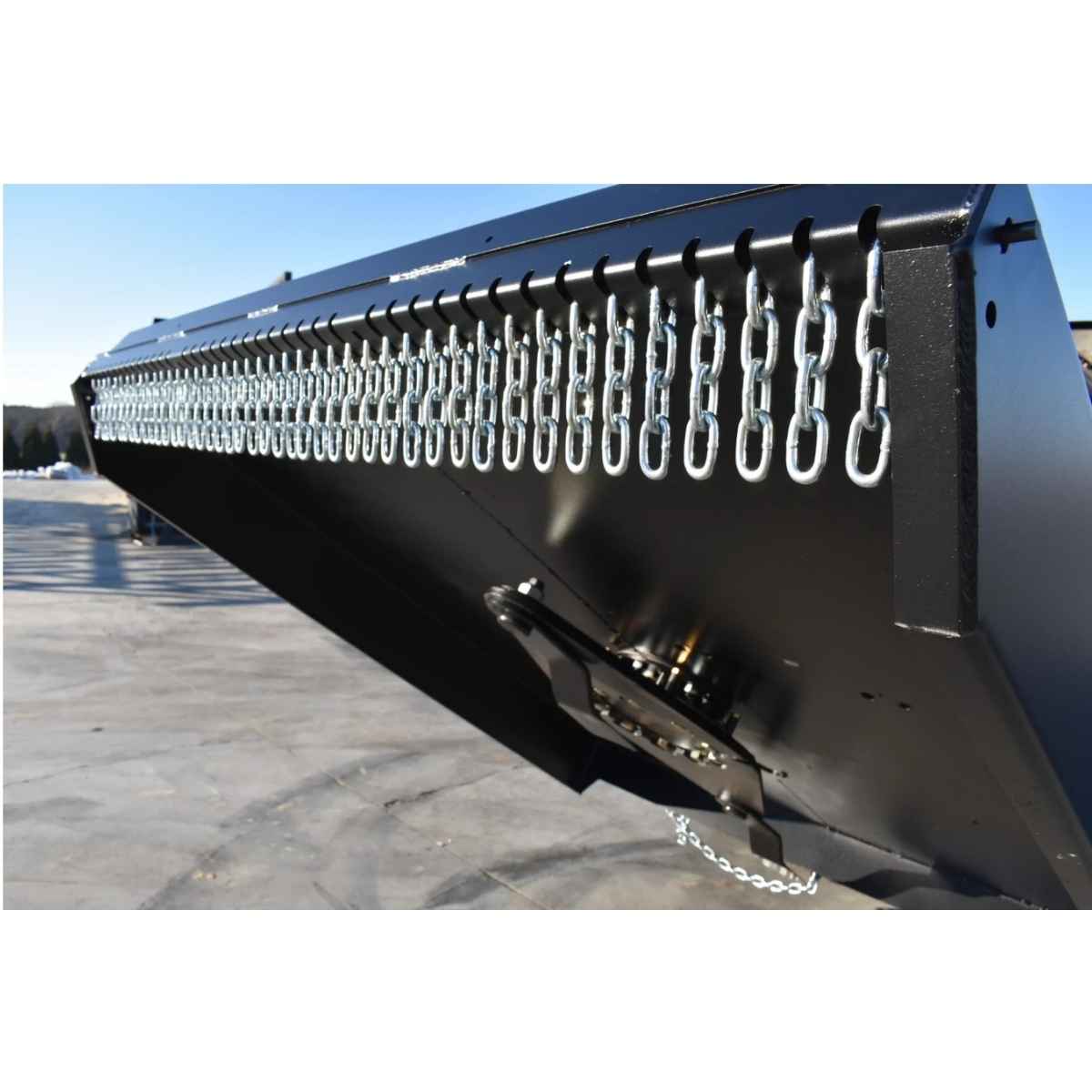 Close-up of a black closed front brush cutter by loflin fabrication with multiple silver hanging chains along the top edge, photographed outdoors on a paved surface under daylight.