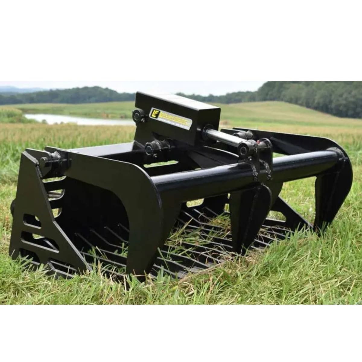 Black loflin skid steer rock grapple on grass with a scenic background