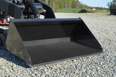 Large black metal loflin fabrication low profile tractor bucket on a construction site with rocks on the ground