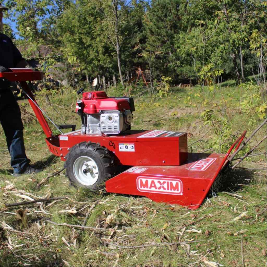 Red Maxim 26 inch brush cutter being used to cut a stump in a grassy area with trees in the background.