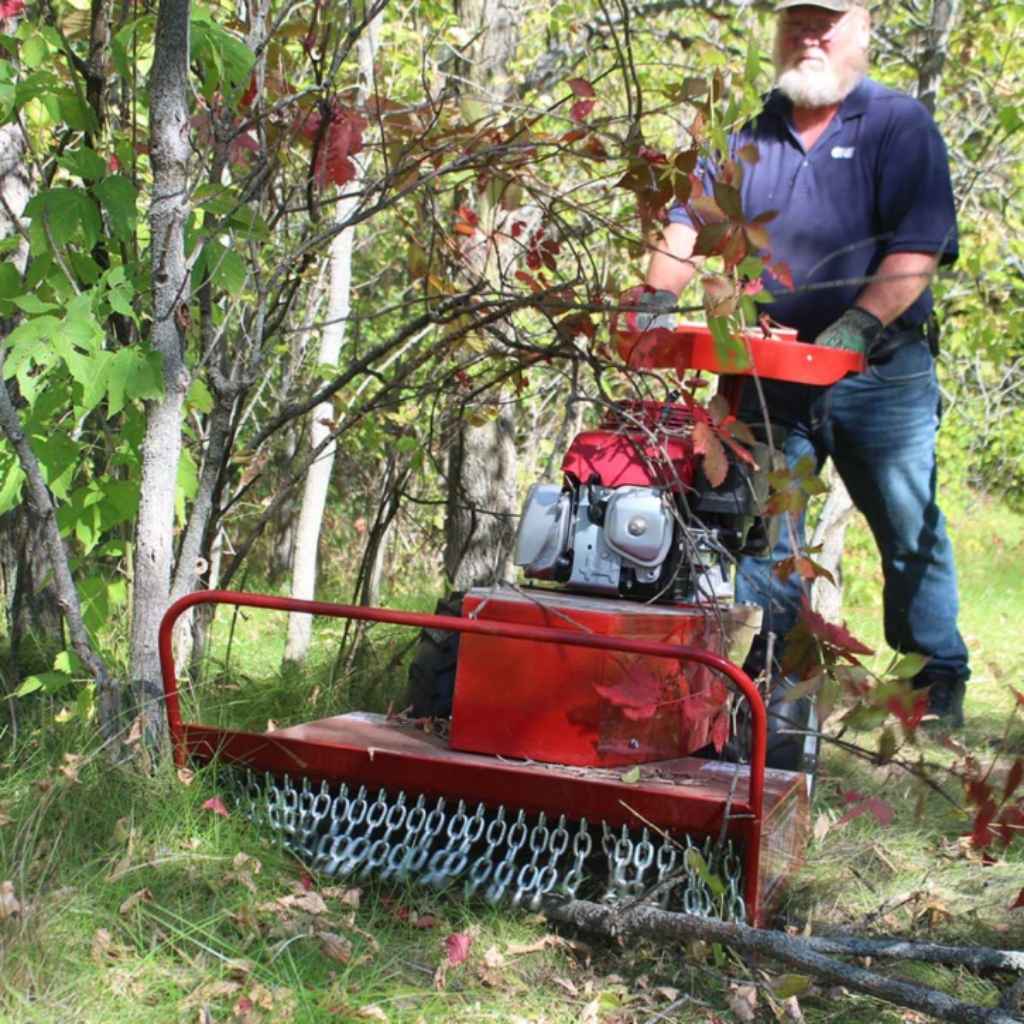 Man operating a red maxim 26 inch brush cutter in a forest setting