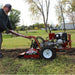 Person operating a red maxim tiller rt190h in a grassy area with trees and buildings in the background.