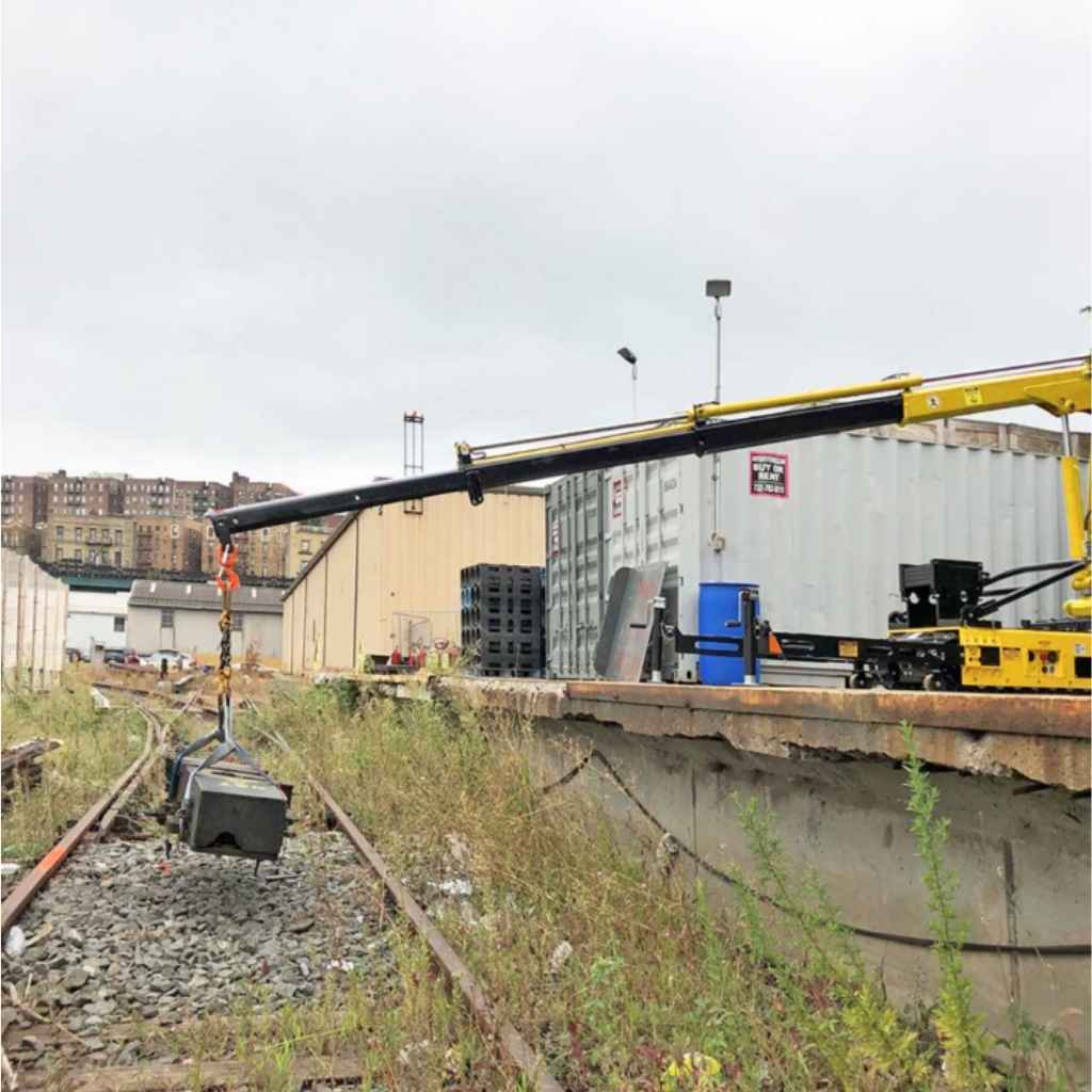 Yellow movex stair climbing crane extended over a railway track with buildings in the background.