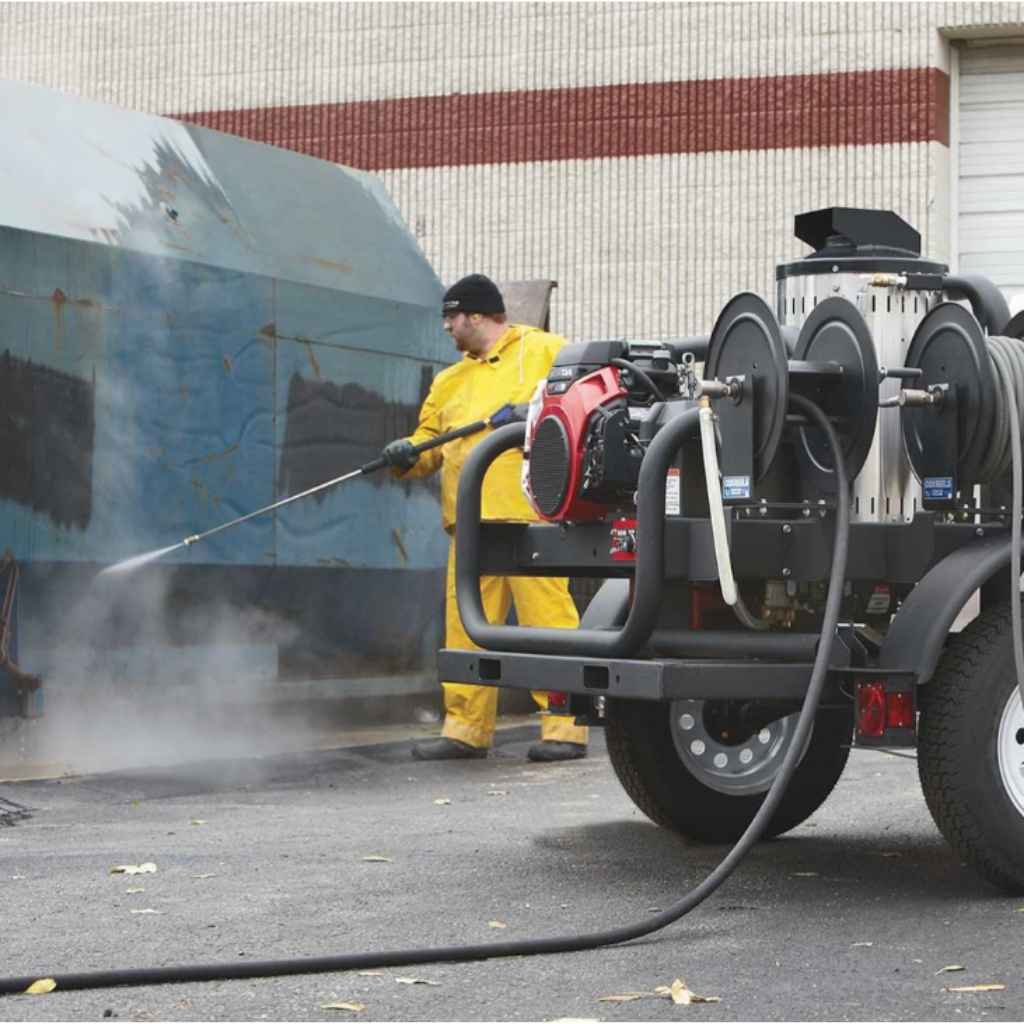 Person using a northstar 4000 psi 4 gpm hot water pressure washer trailer on a vehicle with a power washer truck in the background.