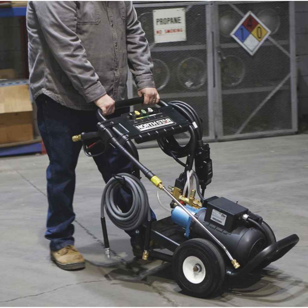 Person pushing a northstar 230v pressure washer with a hose reel in an industrial setting.