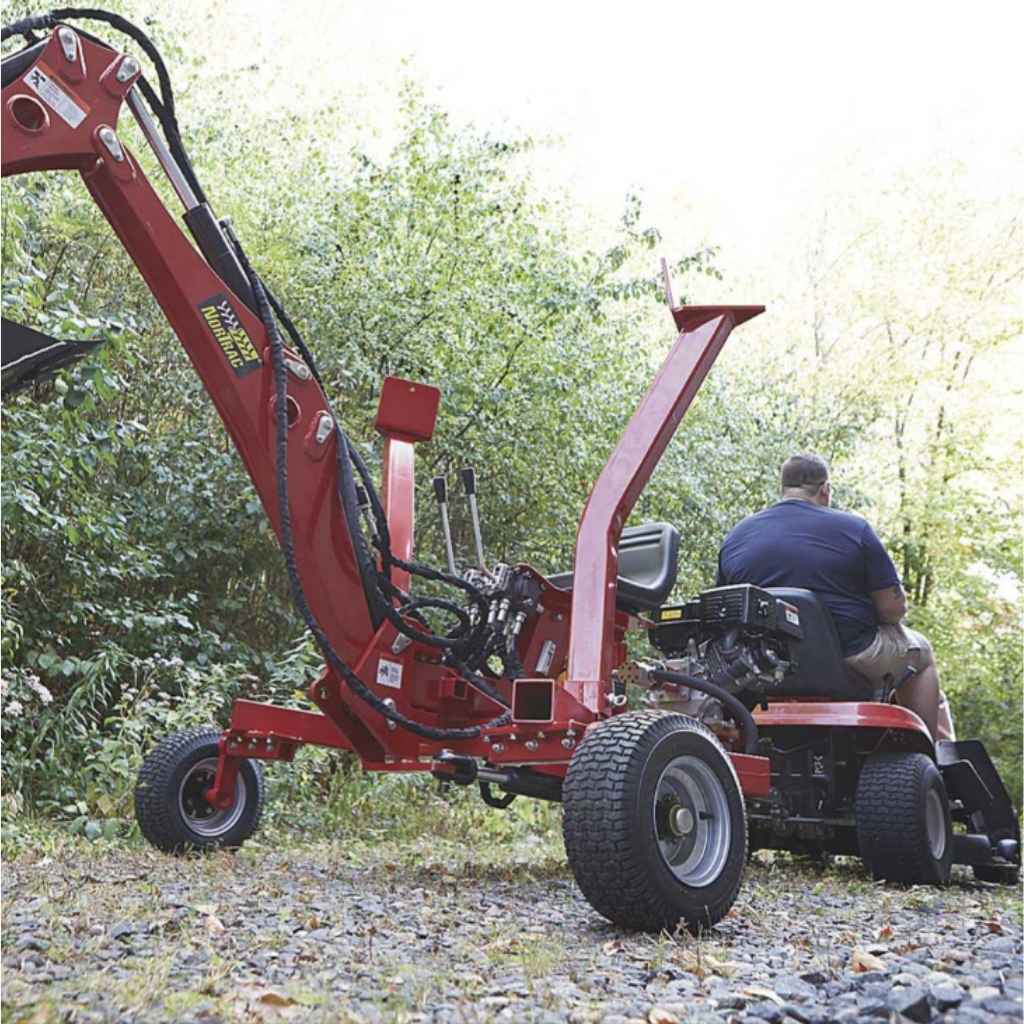 Person operating a red riding lawn mower with a nortrac 15 hp tow behind backhow trencher attached in a wooded area