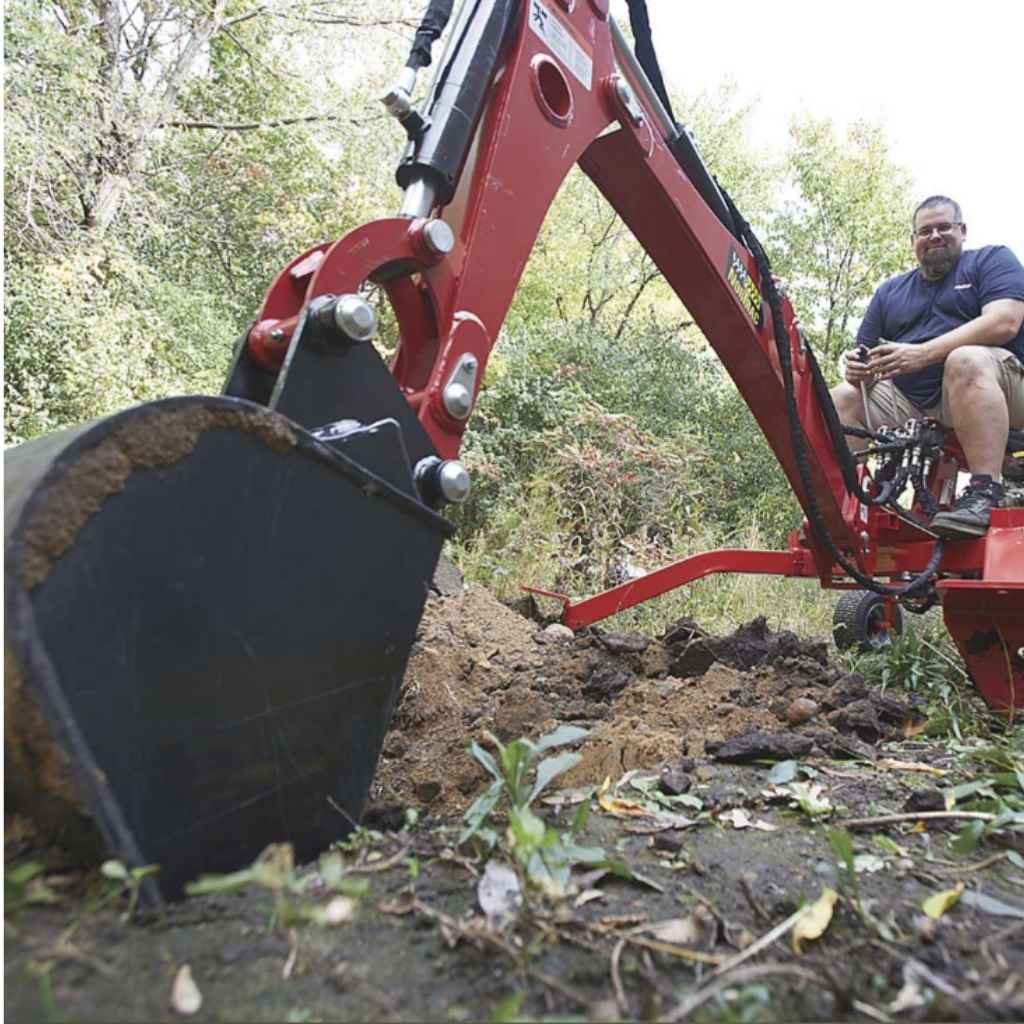 Person operating a red nortrac tow behind backhoe in a wooded area