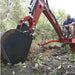 Person operating a red nortrac tow behind backhoe in a wooded area