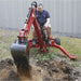 Person operating a red Nortrac tow behind backhoe trencher in a field.