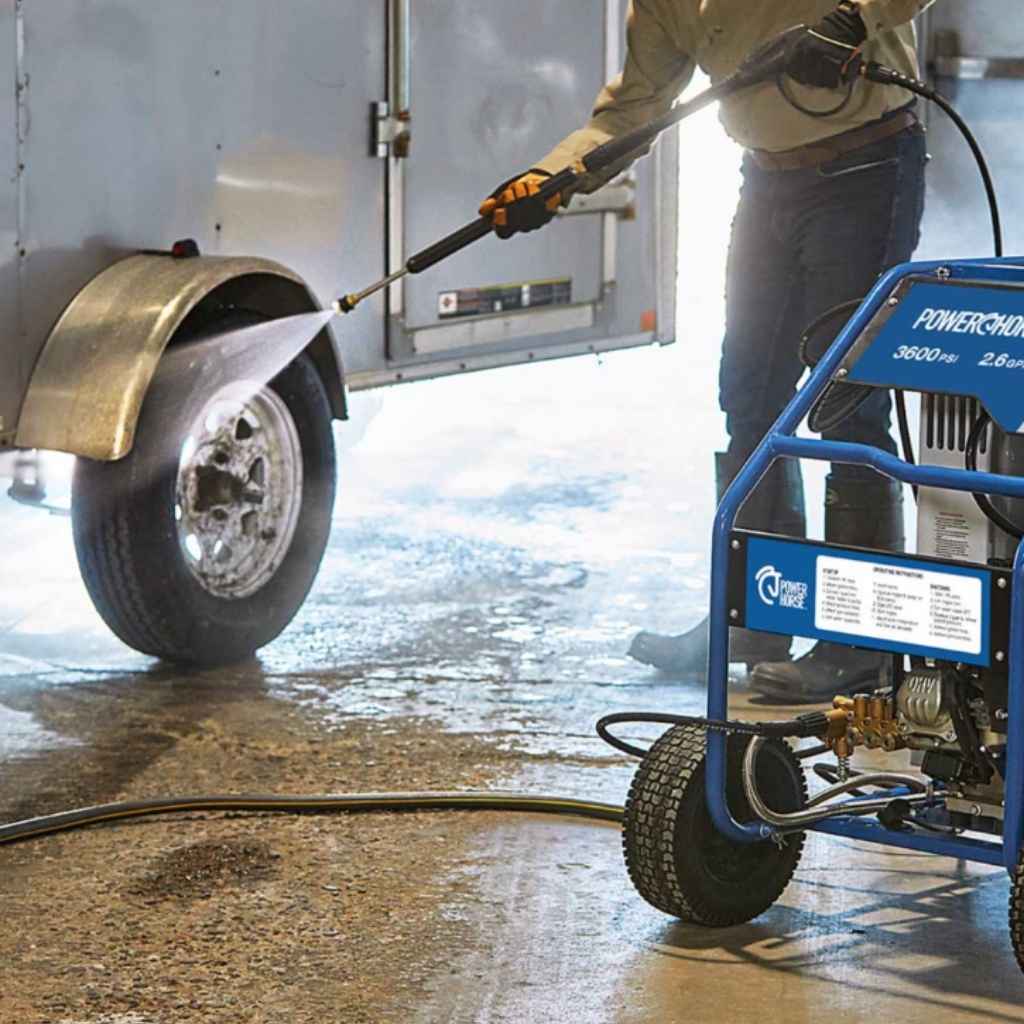 Person using a powerhorse hot water 3600 psi pressure washer to clean a vehicle tire in a garage.