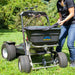 Person using a spyker ride on fertilizer spreader on a grassy area with trees in the background