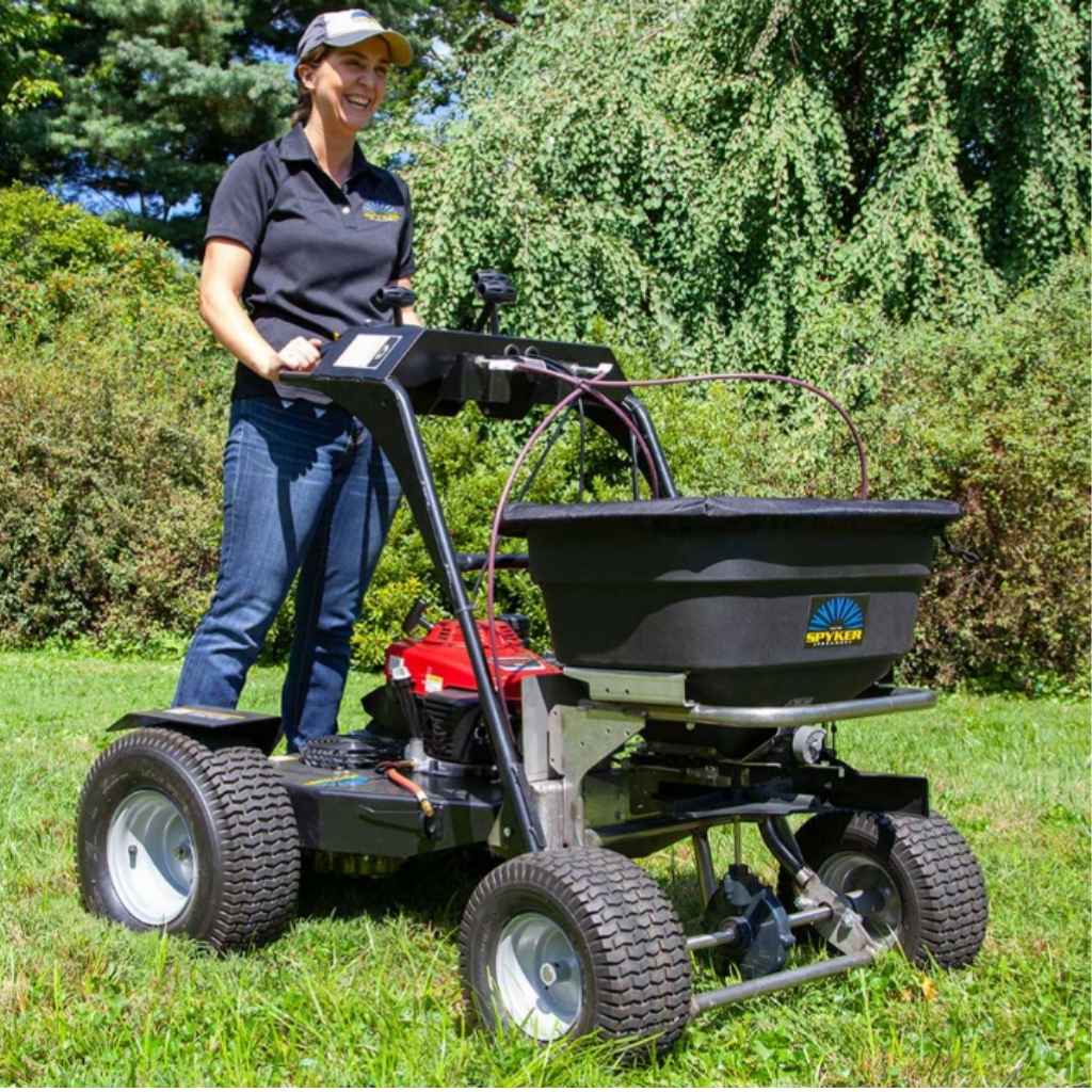 Person operating a spyker ride on fertilizer spreader in a grassy area with trees in the background