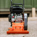 An orange and black plate compactor by superhandy with a gas engine, designed for compacting soil and gravel. Front view outdoors.