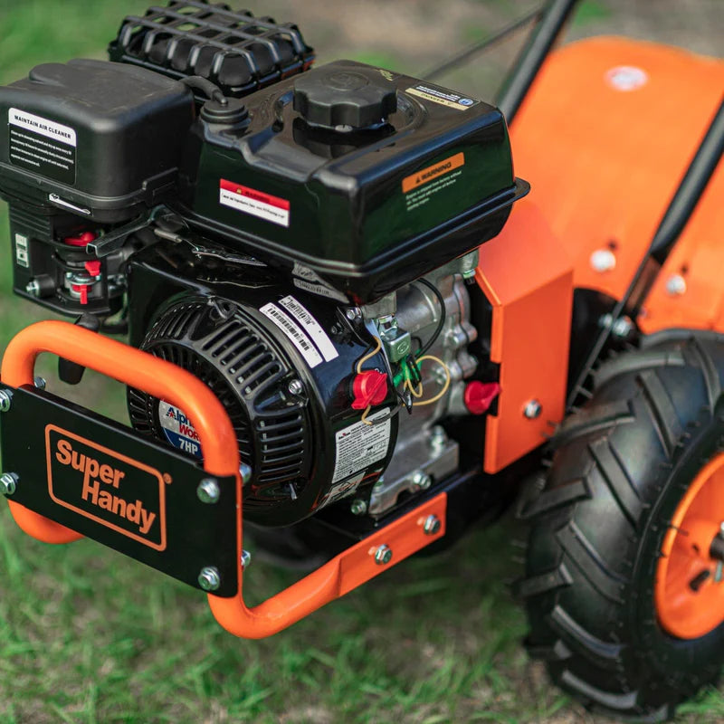 A superhandy 16" rear tine tiller with orange, black, and gray coloring, featuring a gas engine and large wheels for garden soil preparation. Engine view outdoors.