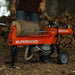 Person operating a SuperHandy electric log splitter 14 ton with a log on it, surrounded by stacked firewood.