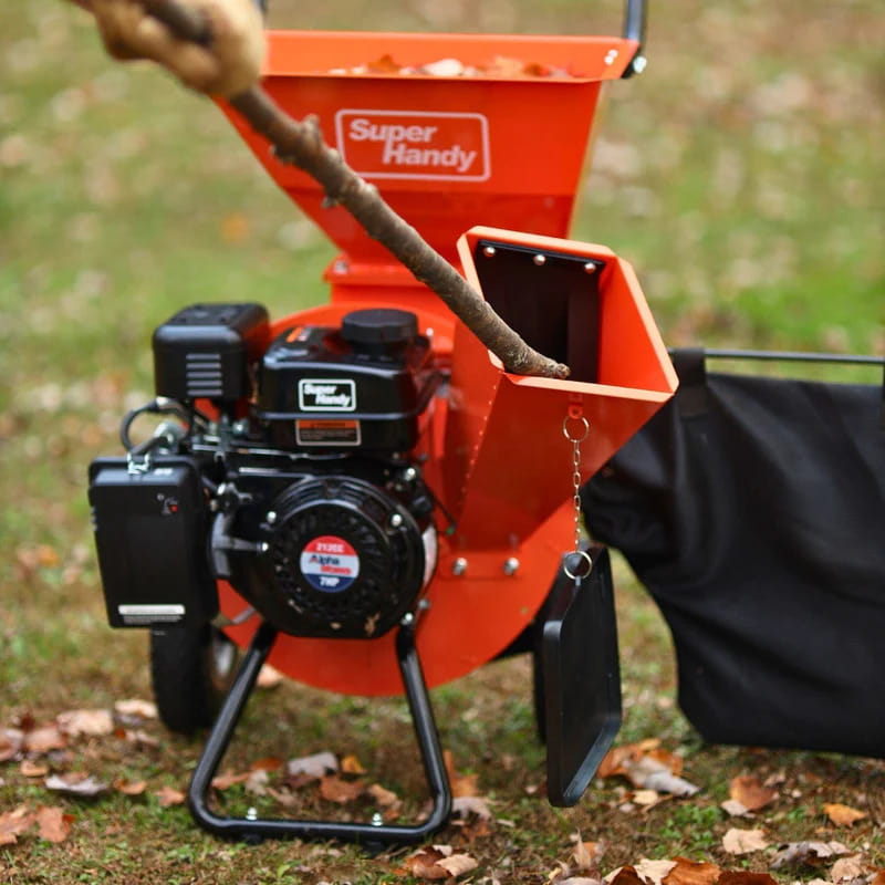Orange and black Super Handy wood chipper pro chipping a branch in a grassy area.