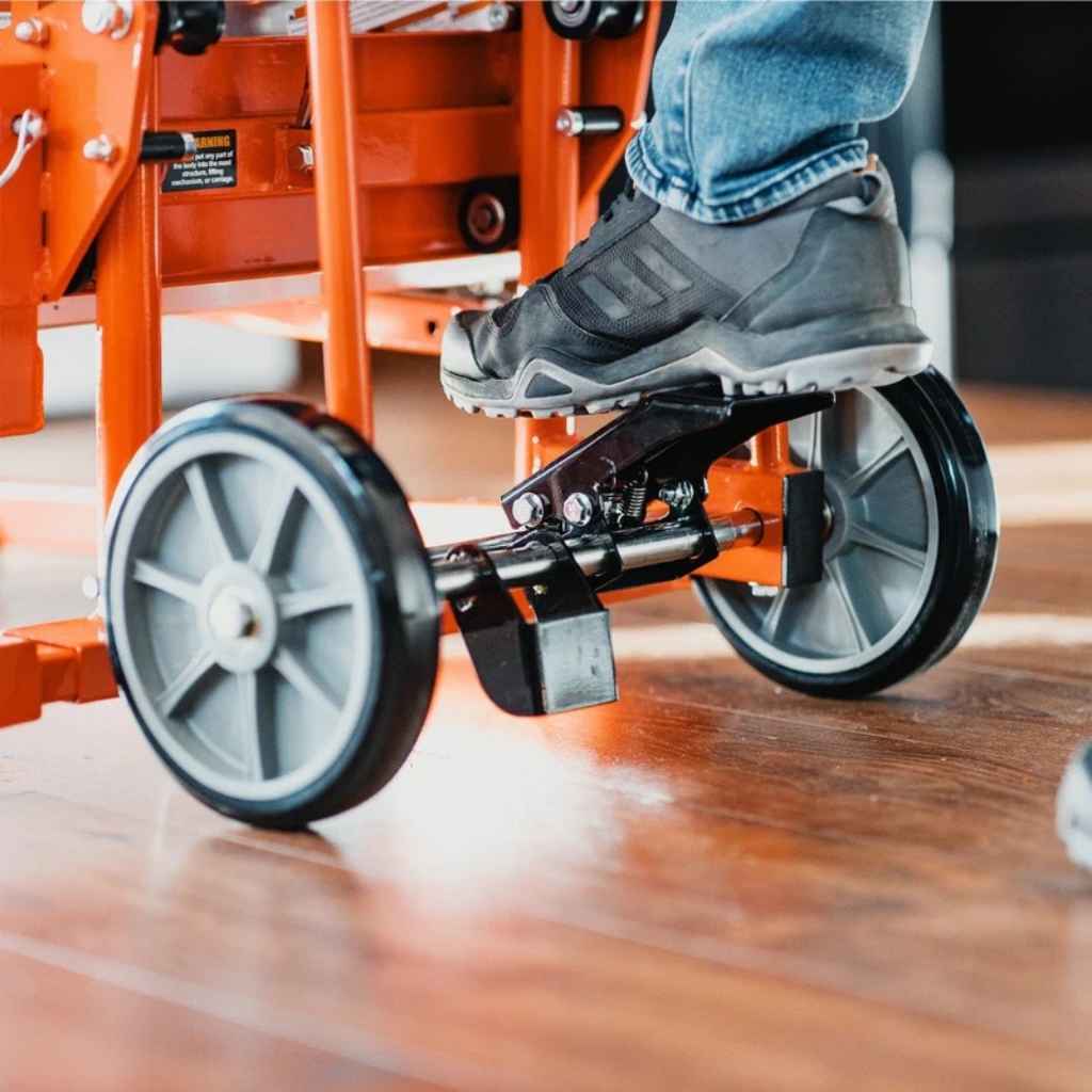 Person using a small orange superhandy material lift with wheels on a wooden floor.