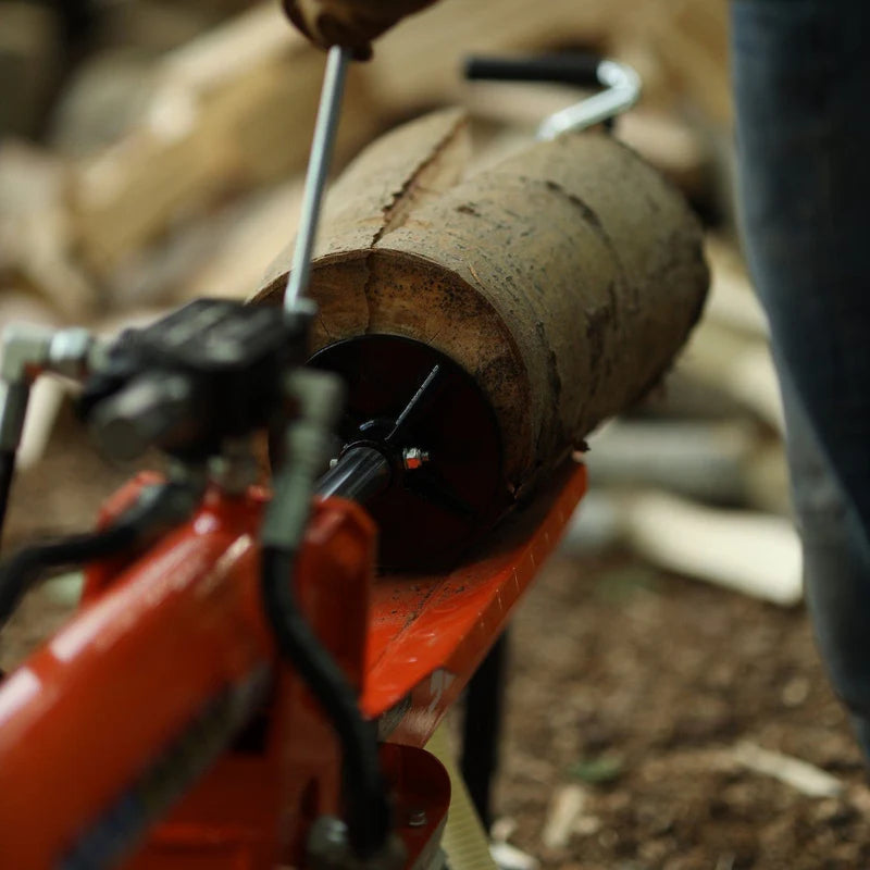 An orange and black 14 Ton Electric Log Splitter with a 20 inch max log length. The equipment is corded and has wheels for mobility. Top back view outdoors in use.