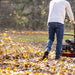 An orange and black SuperHandy walk-behind gas leaf blower with rugged all-terrain wheels and a 209CC gas engine. Back view outdoors in use.