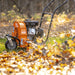 An orange and black SuperHandy walk-behind gas leaf blower with rugged all-terrain wheels and a 209CC gas engine. Side view outdoors in use up close.