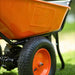 An orange and black superhandy 24v  electric wheelbarrow with a visible 24V 7Ah AGM battery. Wheel view outdoors.