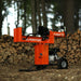 A 25 Ton Gas Log Splitter with a 7HP 209CC engine, colored in orange and black, with a large log placed on its splitting platform. Side view outdoors horizontal position.